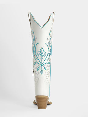 A single white cowboy boot shown from the back, featuring turquoise and silver embroidered floral patterns on the shaft and a tan stacked heel, set against a light gray studio background.