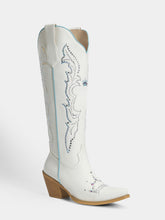 A white leather cowboy boot with decorative blue and silver embroidery, a pointed toe, and a stacked wood-look heel, shown against a light gray background.