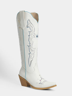 A white leather cowboy boot with decorative blue and silver embroidery, a pointed toe, and a stacked wood-look heel, shown against a light gray background.