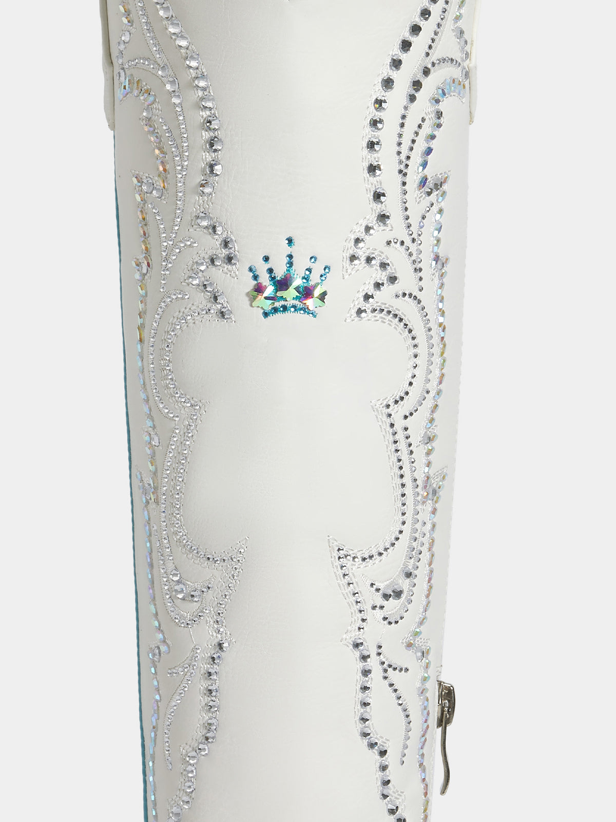 A close-up of a white western boot featuring intricate silver rhinestone scrollwork and a small blue and green crown embellishment near the top.